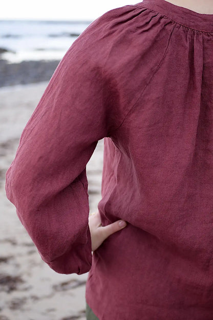 Close-up of a woman wearing a berry long-sleeve top on a beach.