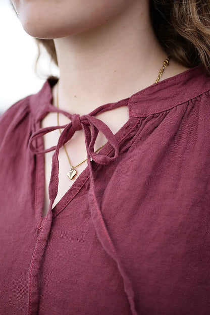 Close-up of a woman wearing a berry top with a tie neckline and gold necklace.