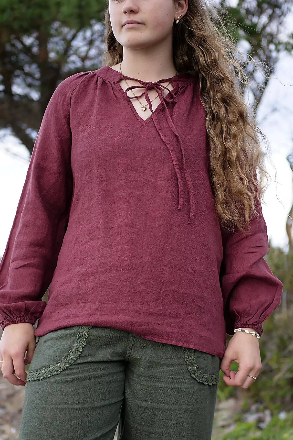 Woman wearing a berry long-sleeve top with a lace-up front, standing outdoors.