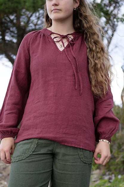 Woman wearing a berry long-sleeve top with a lace-up front, standing outdoors.