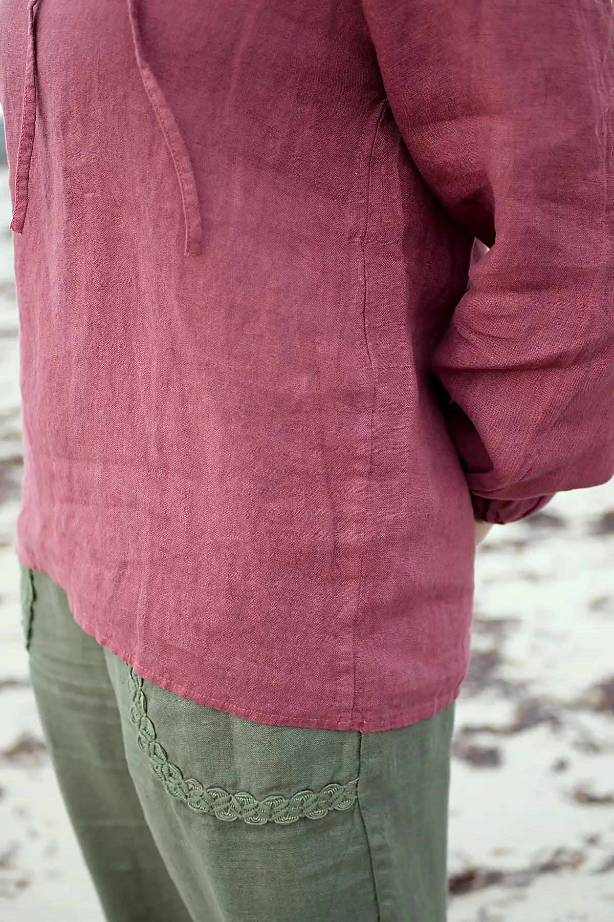Close-up of a woman wearing linen berry top and green pants on a beach.