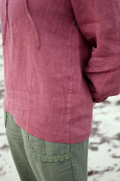 Close-up of a woman wearing linen berry top and green pants on a beach.