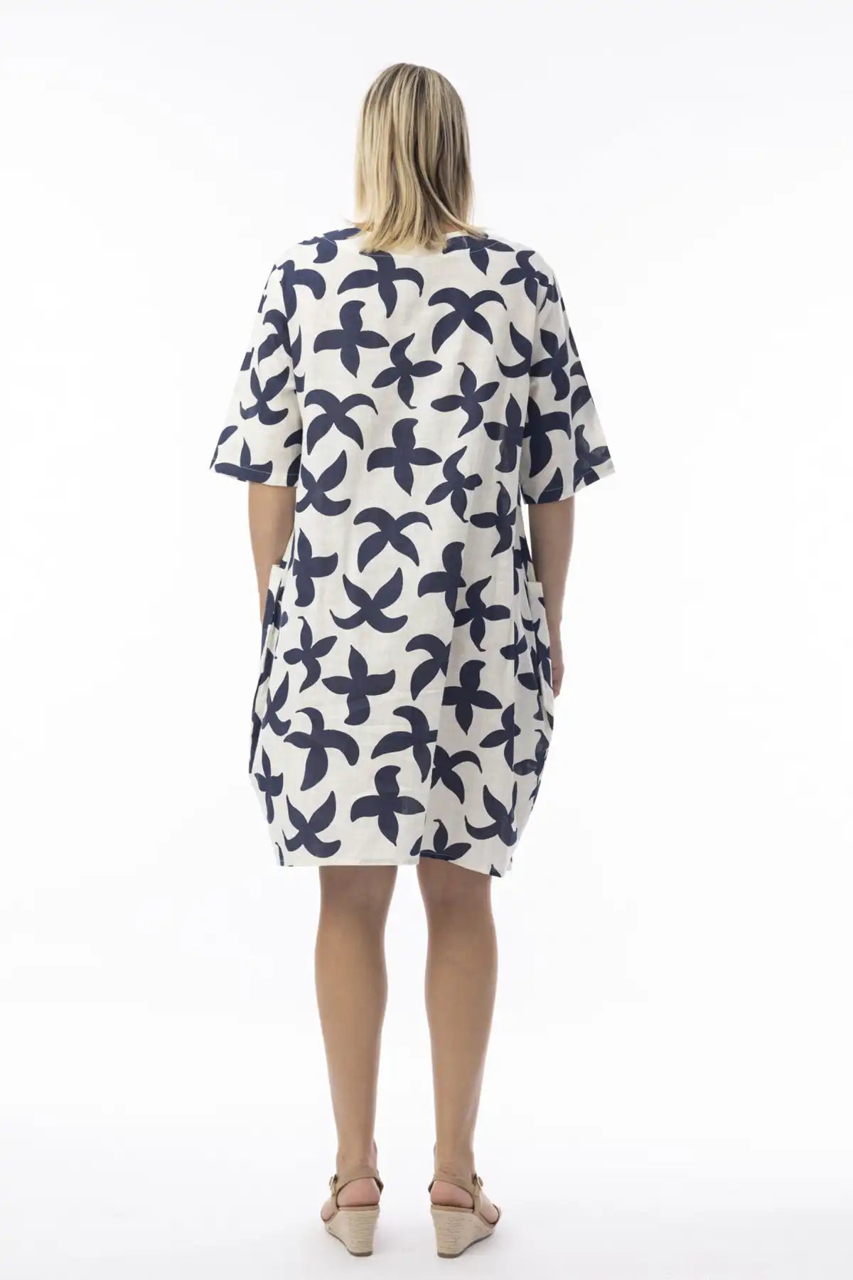 Woman wearing a white dress with blue floral pattern with back to camera on a white background