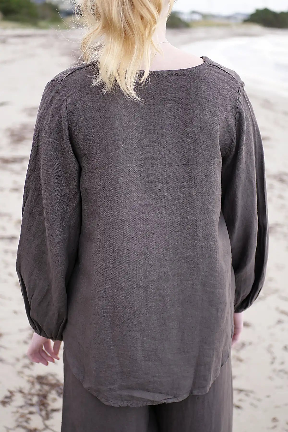 Person wearing a dark gray long-sleeve top on a sandy beach.