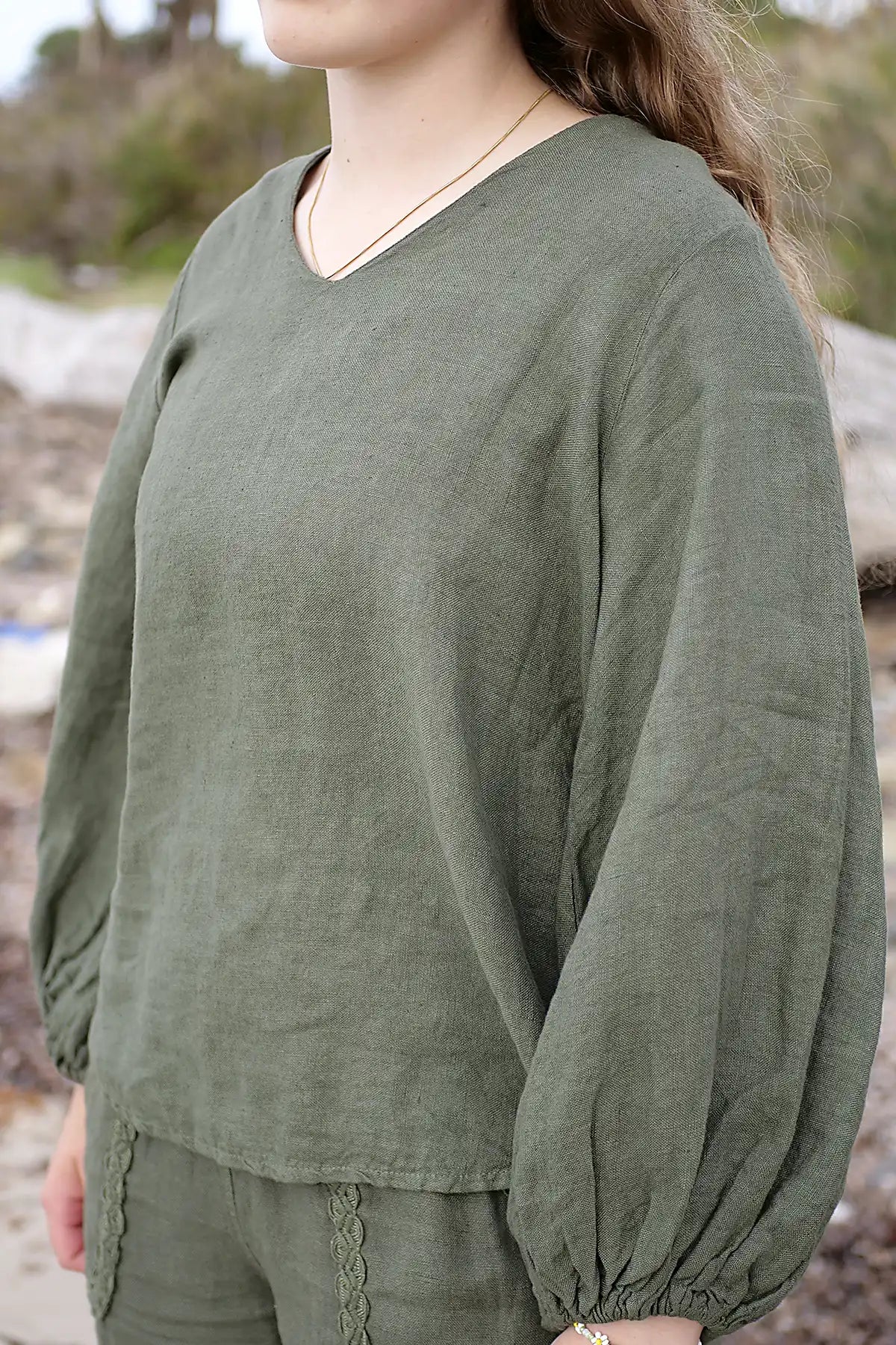 Person wearing a green long-sleeve top with a blurred natural background