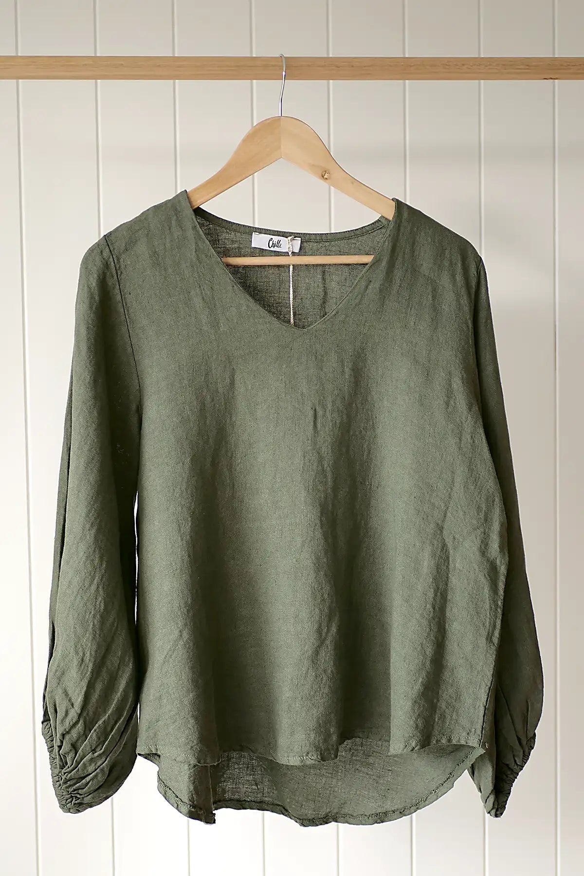 Green blouse on a wooden hanger against a white paneled wall