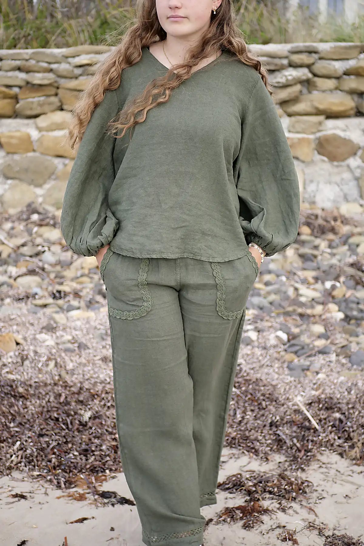 Person wearing an olive green outfit standing on a rocky beach.
