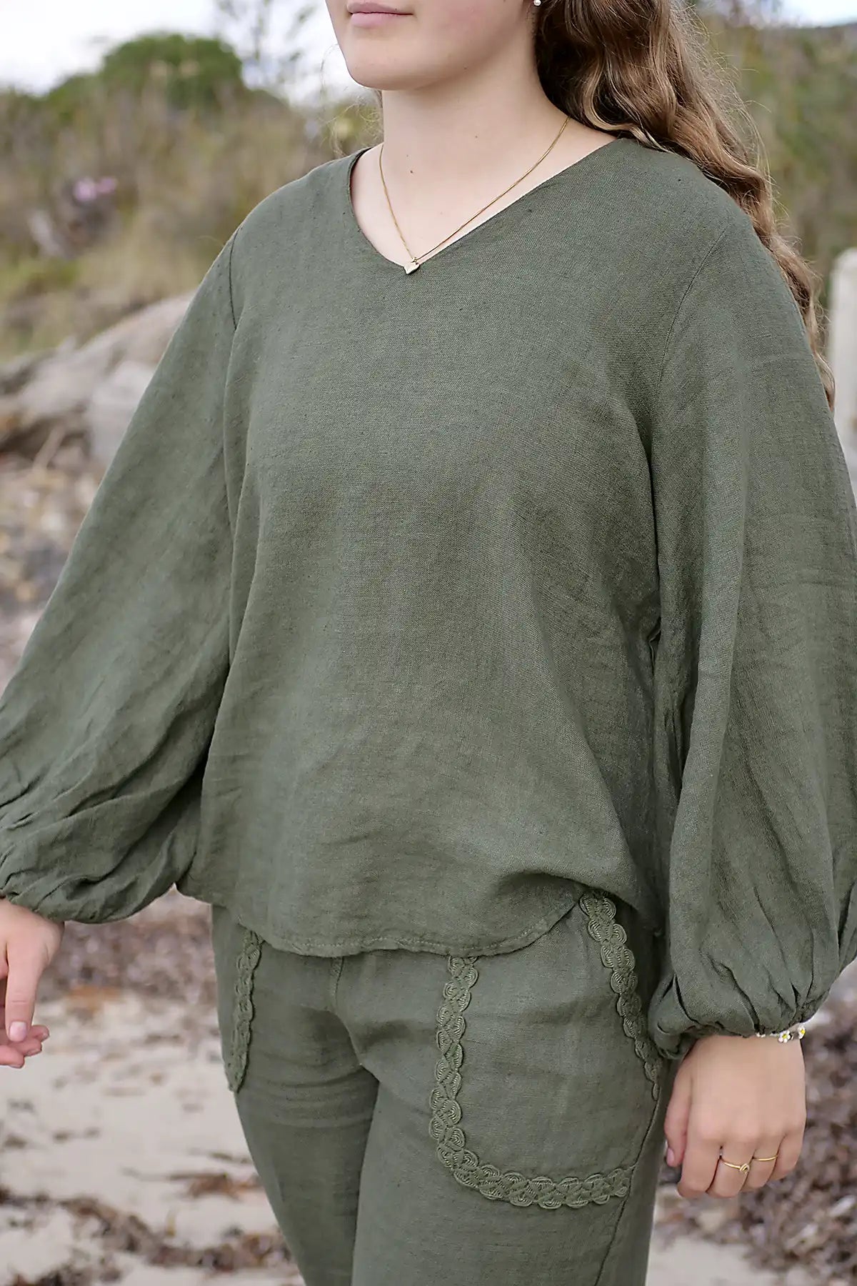 Person wearing an olive green outfit with long sleeves and lace details, standing outdoors.
