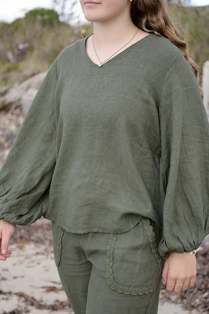 Person wearing an olive green outfit with long sleeves and lace details, standing outdoors.