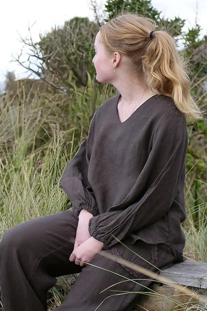 Person wearing a brown outfit sitting on a wooden bench in a natural setting